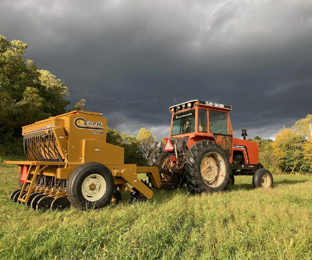 Yellow Esch no-till drill attached to a red tractor in a grassy field.