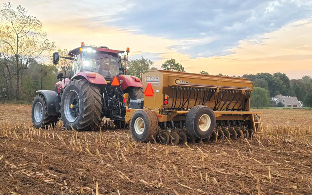 Red tractor pulling a yellow Esch drill through a harvested field.
