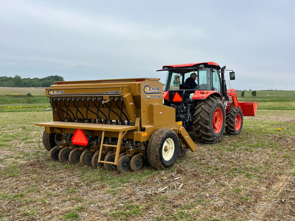 Yellow Esch no-till drill attached to a red tractor in a field.
