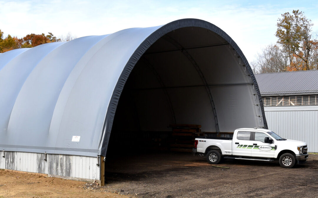 White fabric hoop building with an open front and a pickup truck at the entrance.
