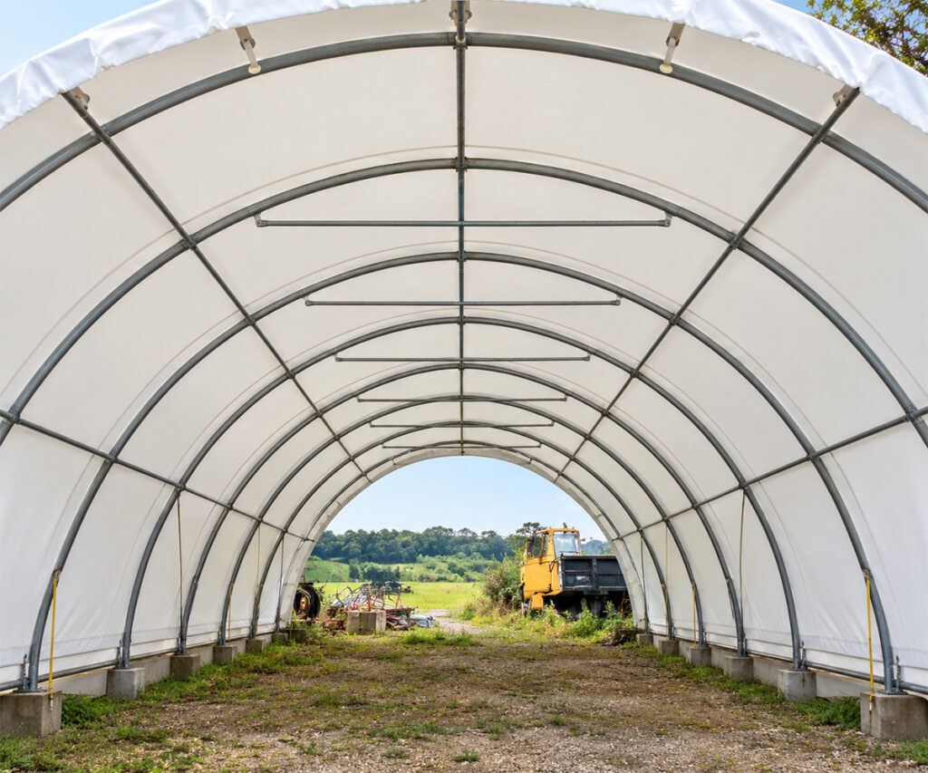 Interior of an empty fabric hoop building showing arched framing and a grassy floor.